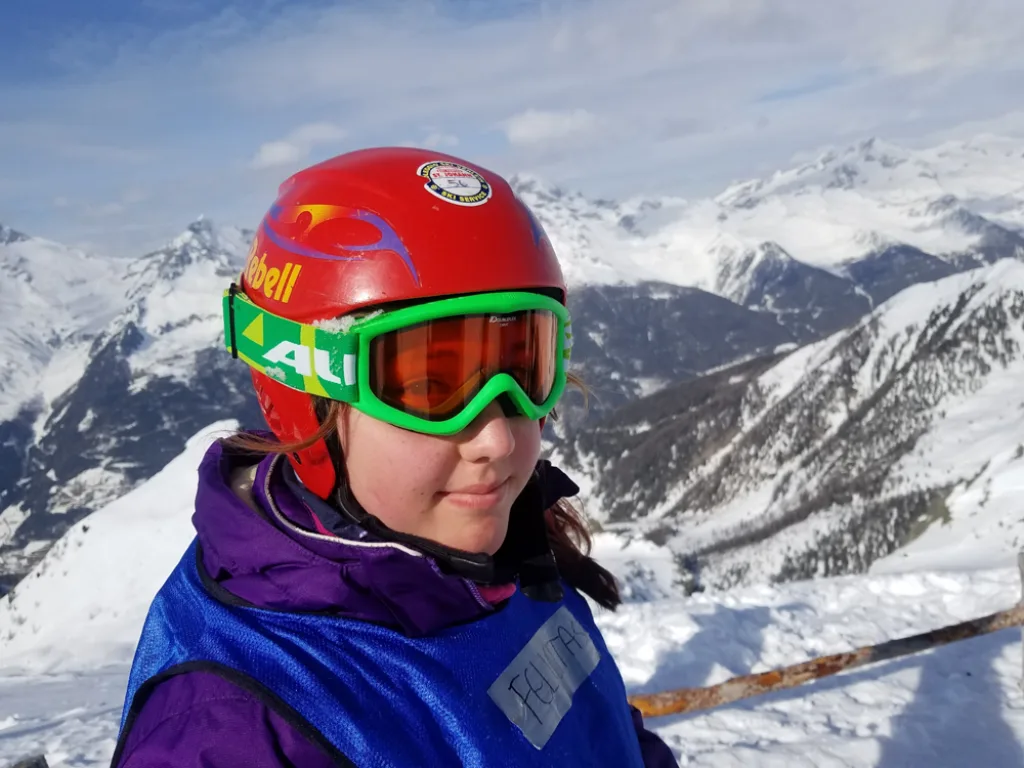 Jugendliche mit rotem Helm und grüner Skibrille im Profil.